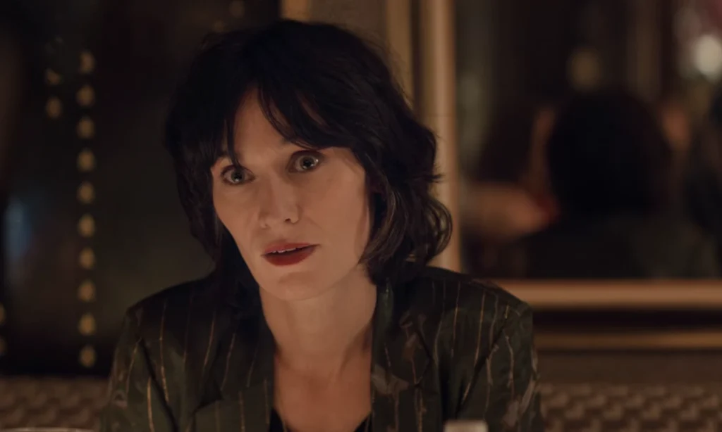 Juliette Pellegrini seated inside a restaurant with a focused expression in Netflix's Lupin.