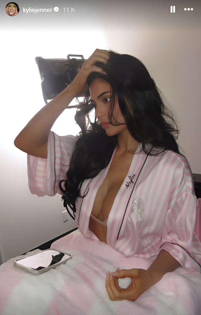Kylie Jenner backstage in a pink-and-white striped Victoria's Secret satin robe with her hair styled in loose waves.