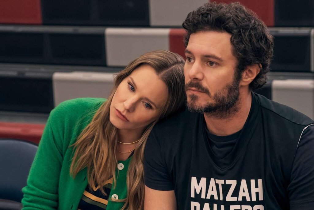 Kristen Bell as Joanne resting her head on Adam Brody as Noah's shoulder, with Noah wearing a "Matzah Ballers" shirt in a scene from Nobody Wants This Season 3.
